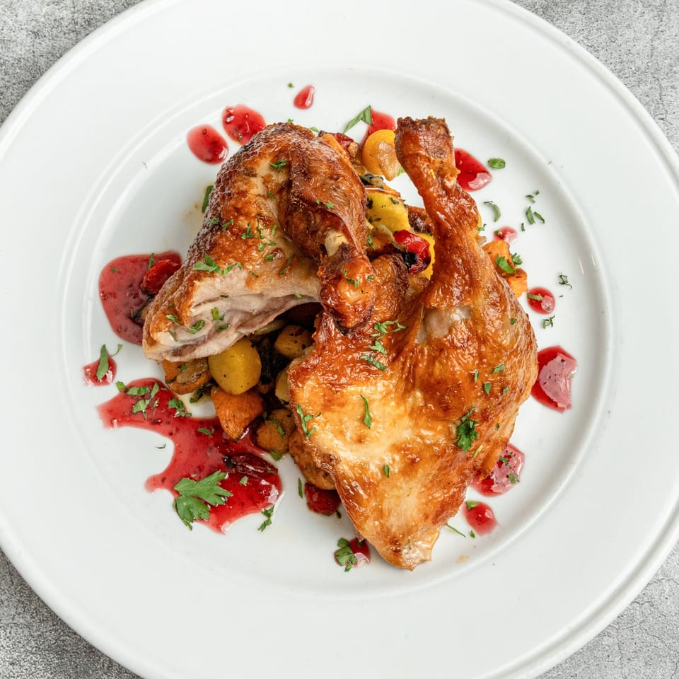 Crispy roasted chicken with vegetables and a red berry sauce on a white plate.
