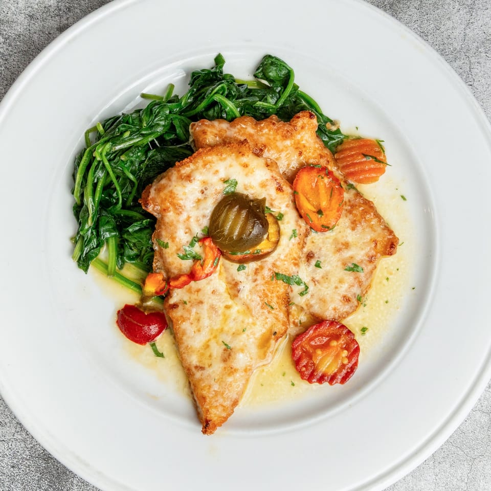 Nosh Kitchen & Cocktails' chicken dish with melted cheese, spinach, and roasted tomatoes on a white plate.
