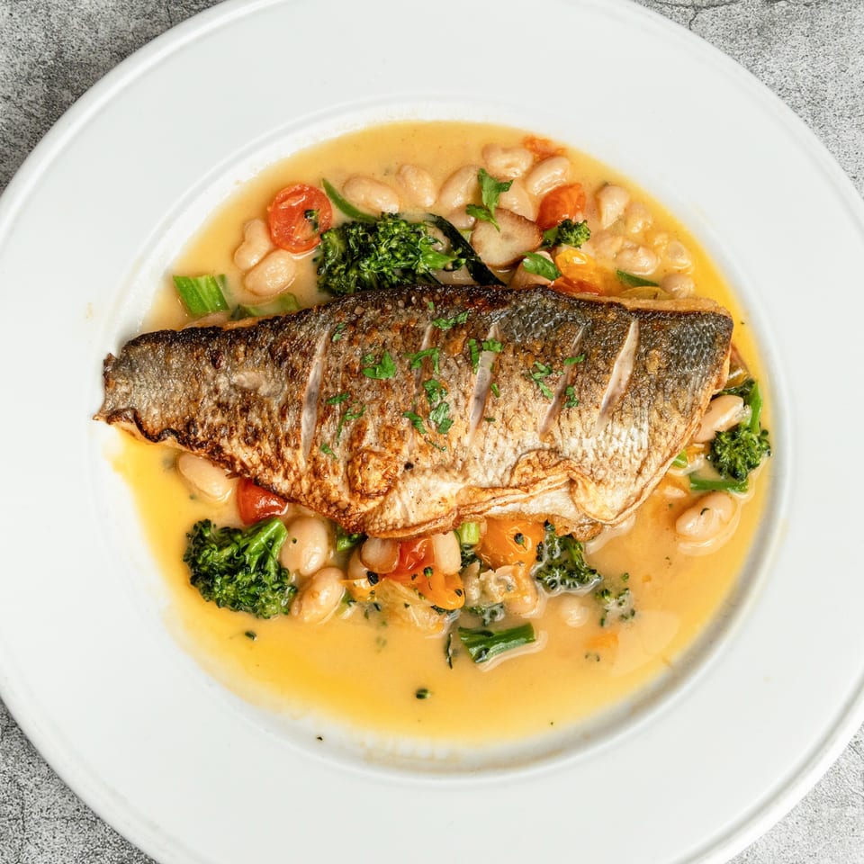 Pan-seared fish with crispy skin, white beans, broccoli, and cherry tomatoes in a light broth.