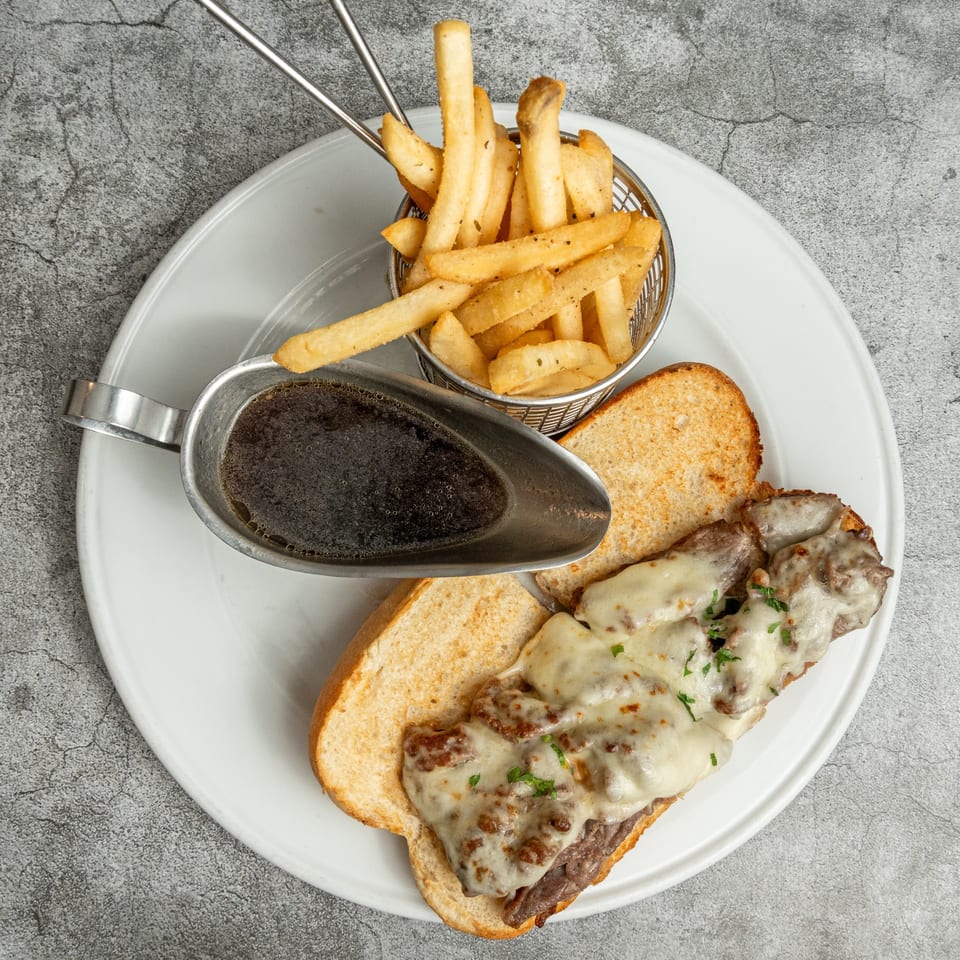 Nosh Kitchen & Cocktails' French dip sandwich with melted cheese, a side of fries, and au jus.