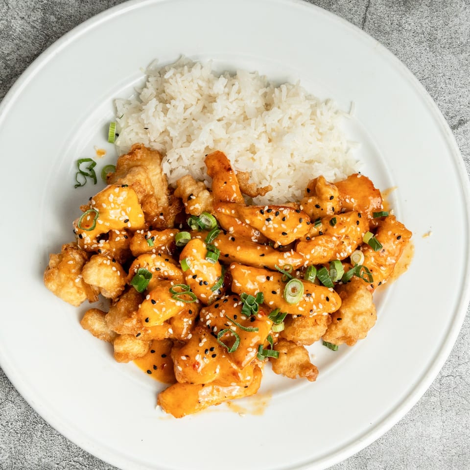 Nosh Kitchen & Cocktails' orange chicken with white rice, garnished with sesame seeds and scallions.