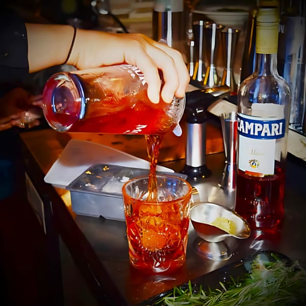 A bartender at Nosh Kitchen & Cocktails pours a red cocktail into a glass with ice.