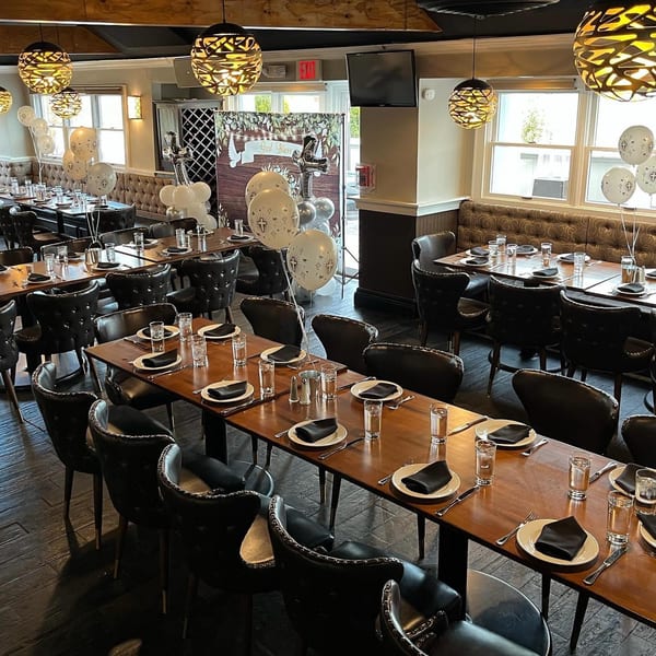 Nosh Kitchen & Cocktails dining room set for an event, featuring long wooden tables, black chairs, and balloons.