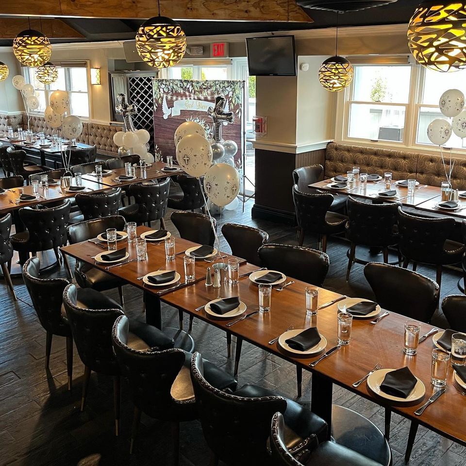 Nosh Kitchen & Cocktails dining room set for an event, featuring long wooden tables, black chairs, and balloons.