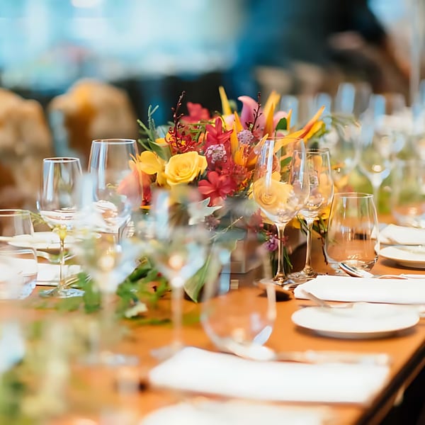 Elegant table setting with wine glasses, white plates, and a vibrant floral centerpiece at Nosh Kitchen & Cocktails.