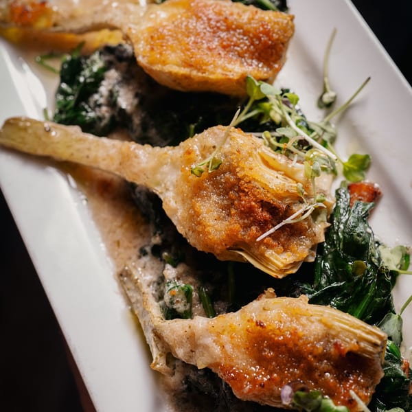 Nosh Kitchen & Cocktails' fried artichoke hearts with sautéed spinach and microgreens on a white plate.
