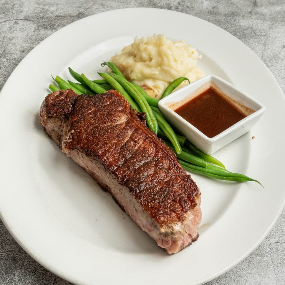 Nosh Kitchen & Cocktails' steak with green beans, mashed potatoes, and a side of gravy.