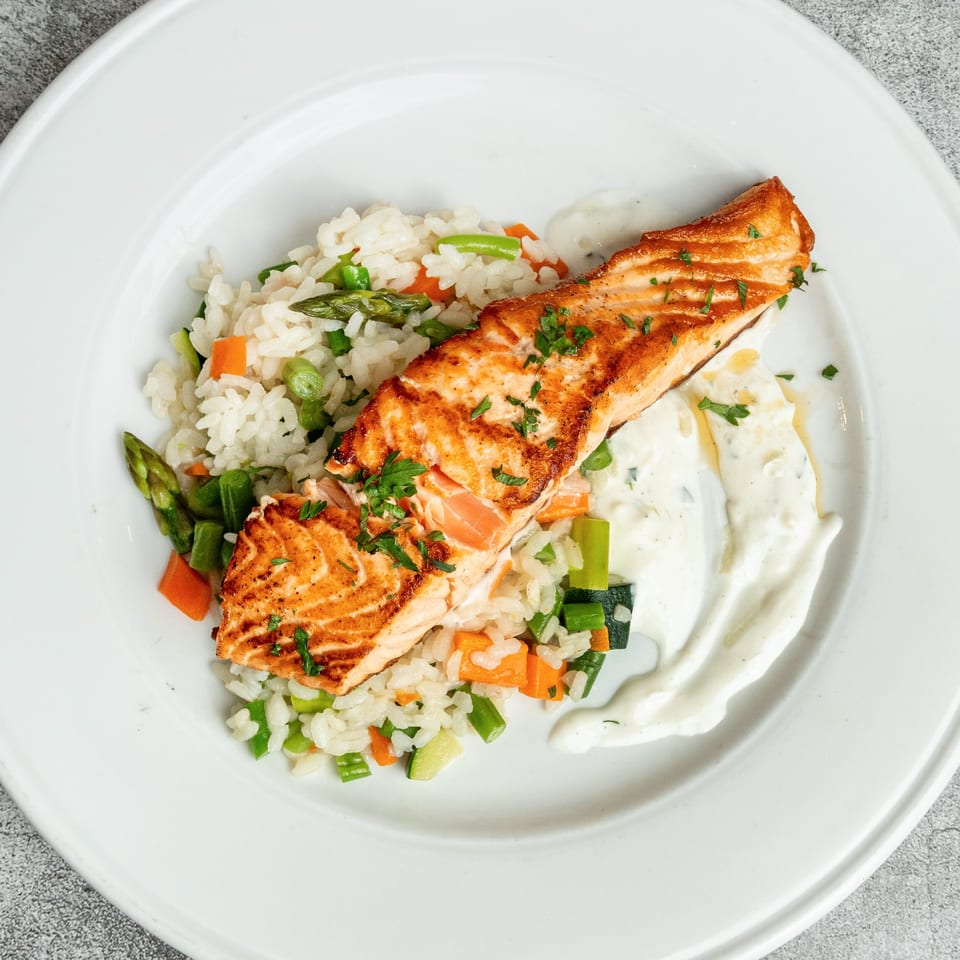Pan-seared salmon fillet with rice pilaf, asparagus, carrots, and a creamy white sauce.